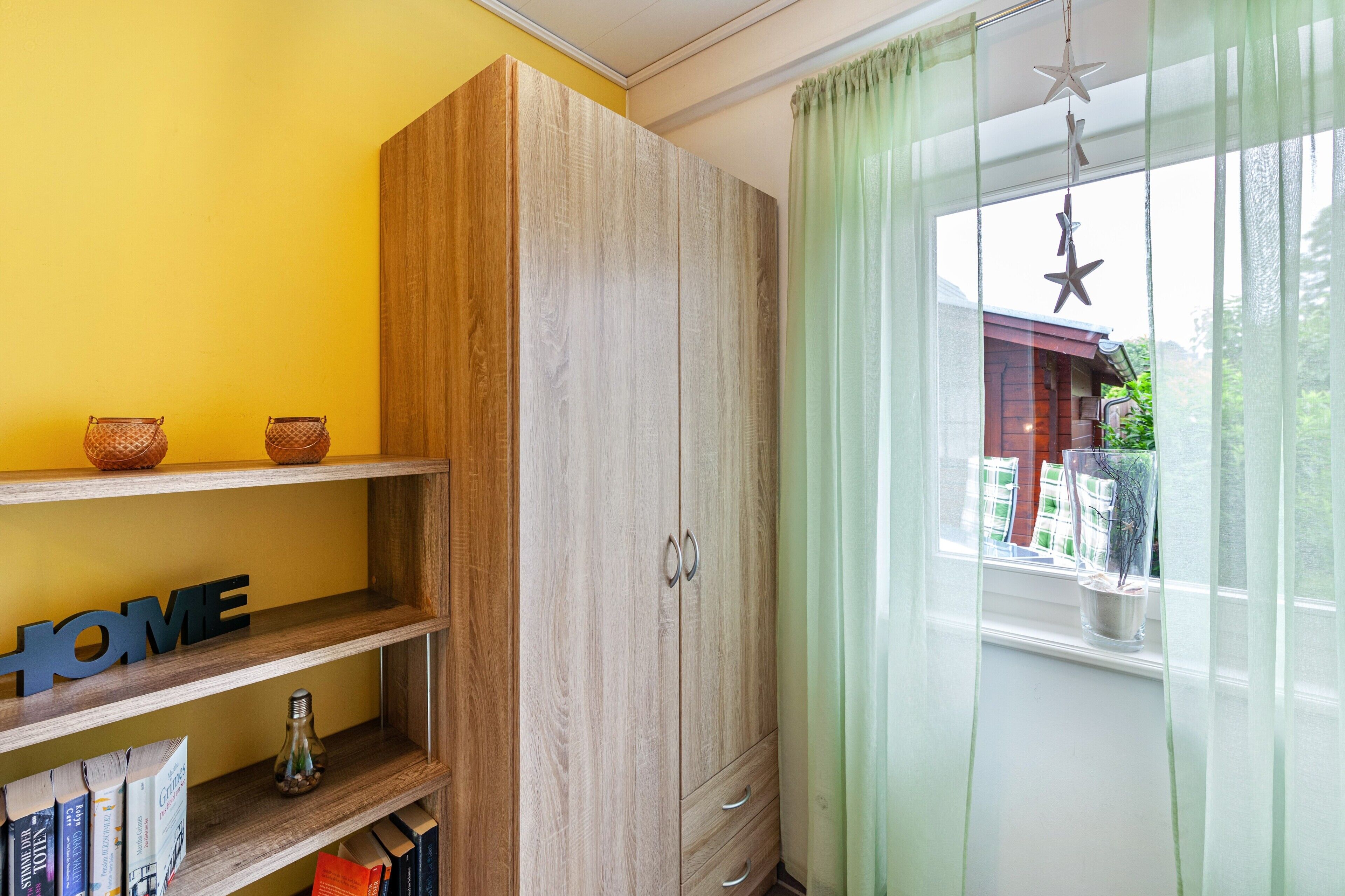Una habitación con un armario de madera, una estantería con libros, un letrero que dice 'HOME' y una ventana con vista a un edificio.