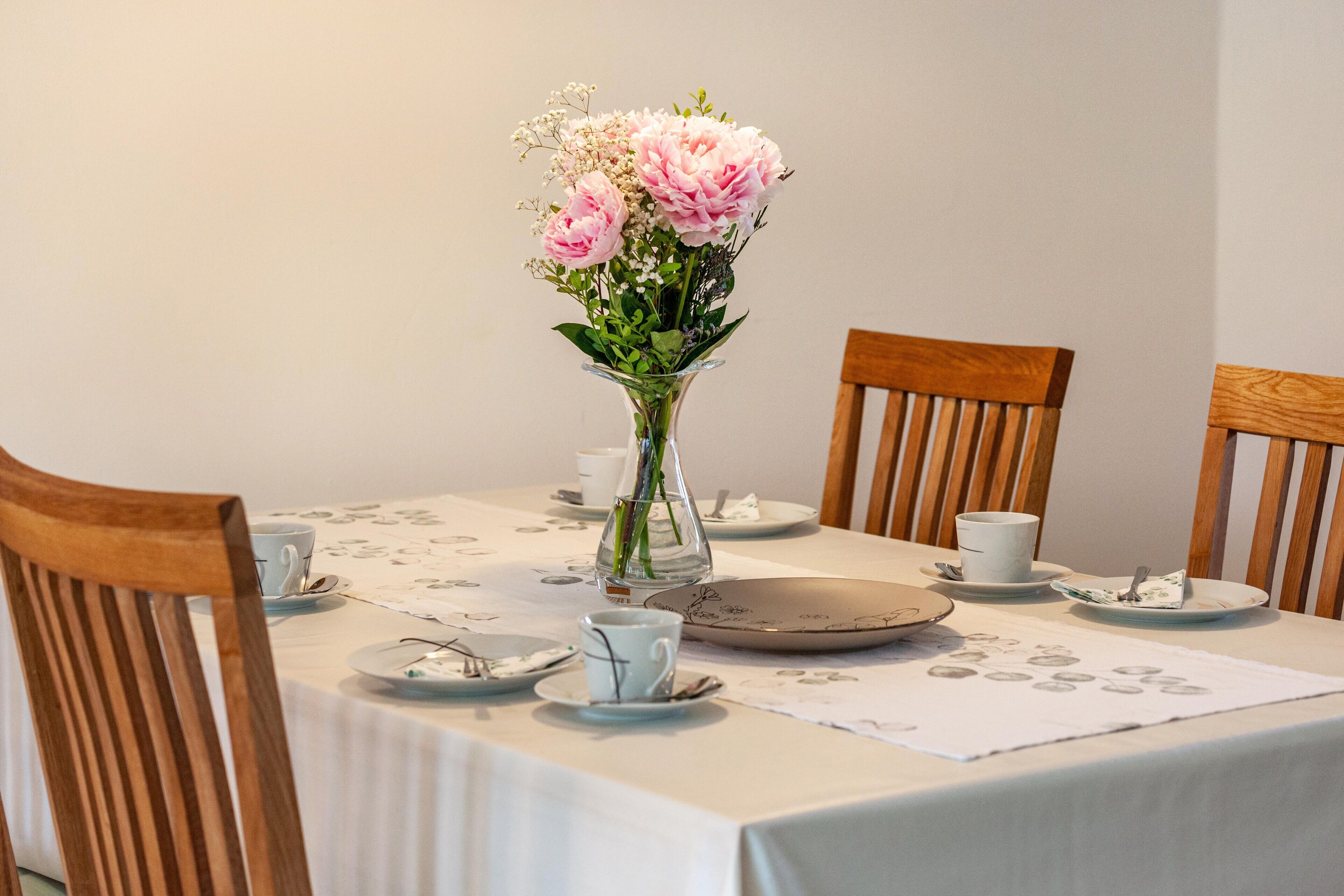 A dining table with a floral centerpiece, white tablecloth, and wooden chairs.