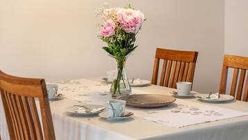 A dining table with a floral centerpiece, white tablecloth, and wooden chairs.