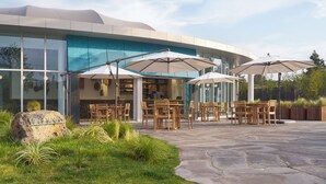A modern building with a glass facade, outdoor seating area with wooden tables and chairs, and umbrellas. - STARVILLE (Seogwipo)
