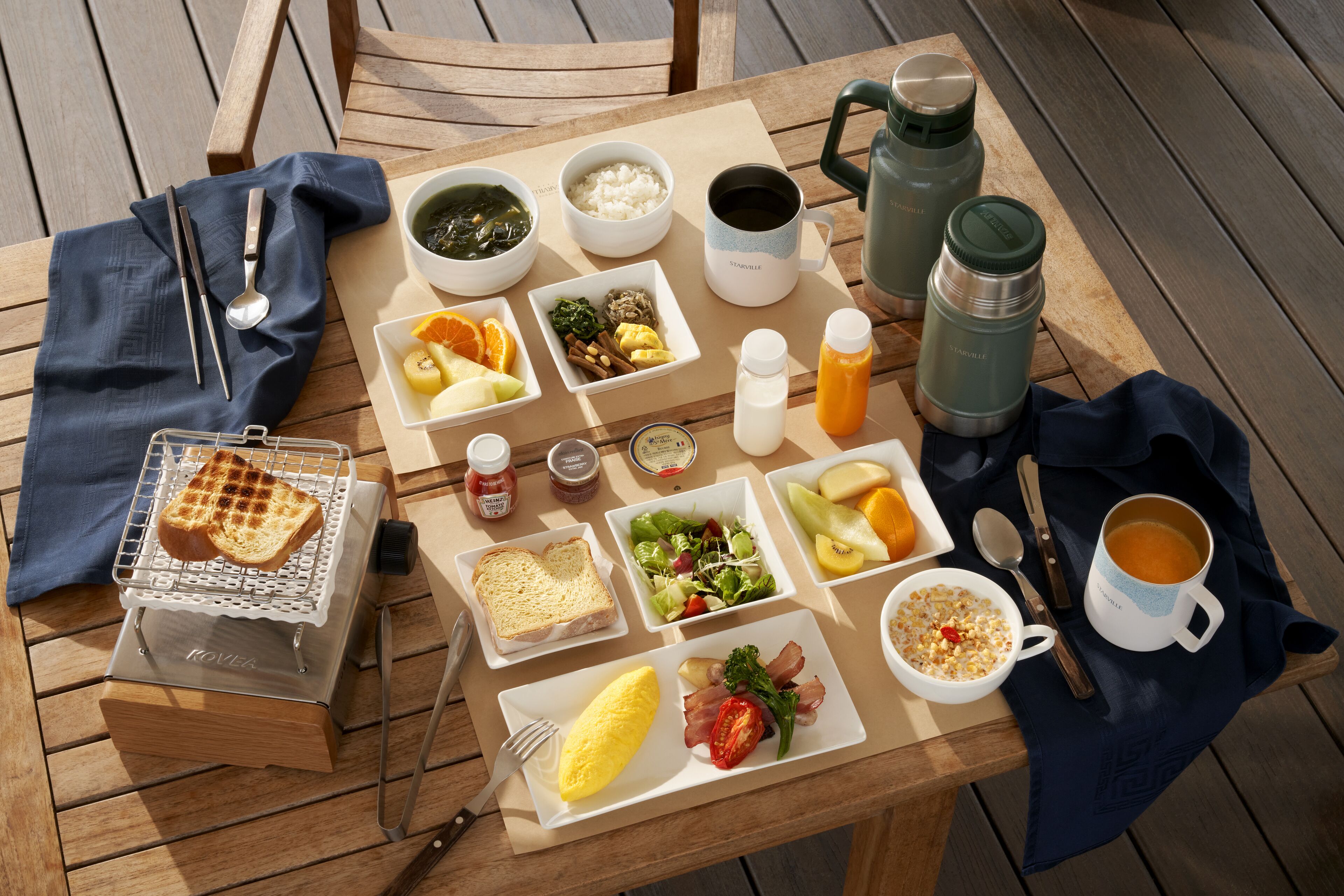 Ein Holztisch, reichhaltig mit Frühstücksleckereien wie Toast, Eiern, Speck und Obst gedeckt.