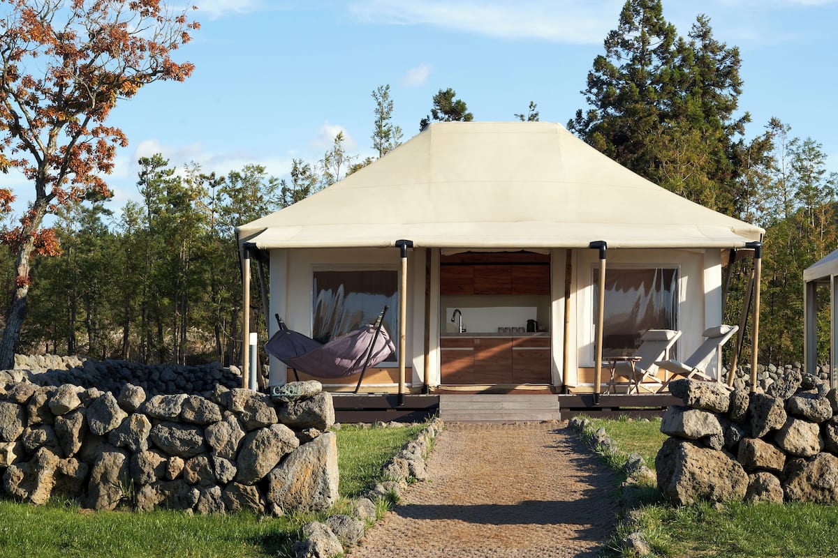 A tented structure with a kitchen area, two lounge chairs, and a stone wall.