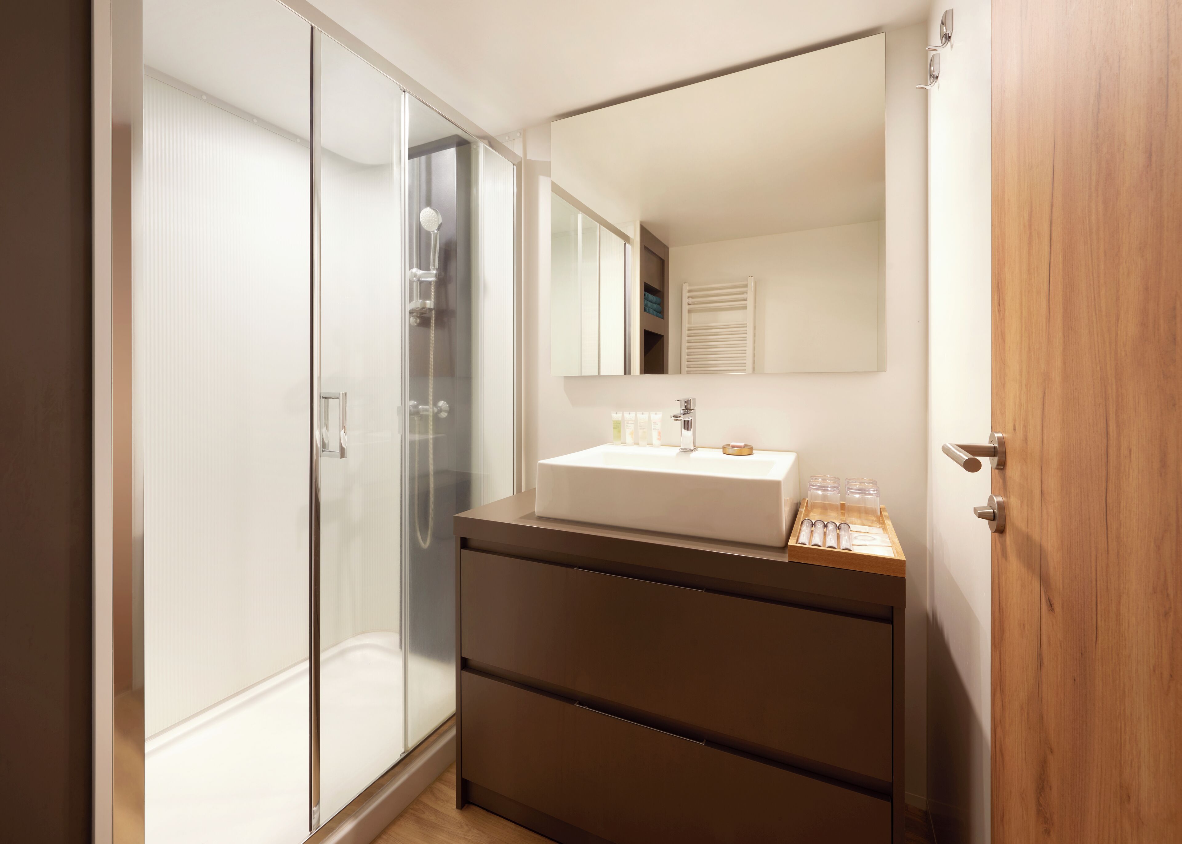 A modern bathroom with a glass shower enclosure, a white sink, and a wooden vanity.