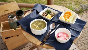 A wooden table with a blue cloth, a bowl of soup, a plate with vegetables and meat, a bowl of fruit, and a wooden box labeled "Starville".