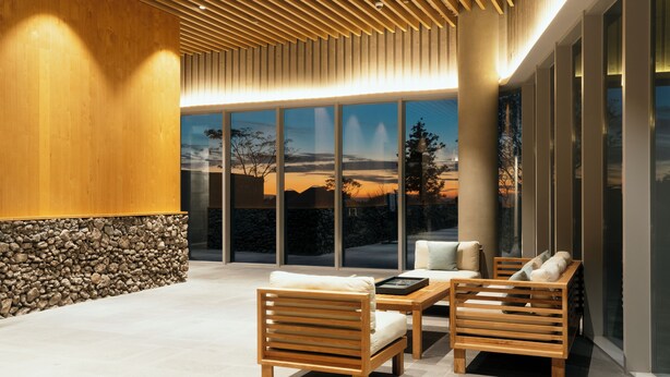 A modern interior with wooden furniture, a stone wall, and large windows offering a view of the outdoors. - STARVILLE (Seogwipo)