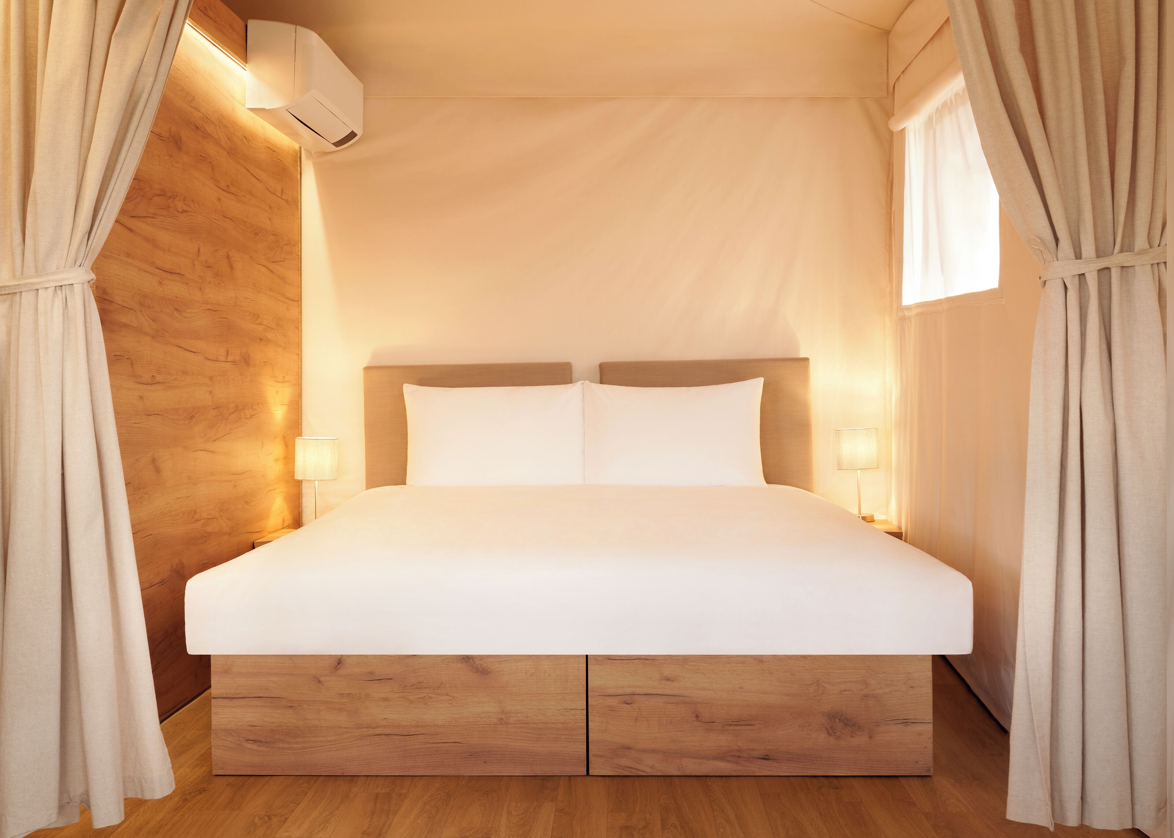 Una cama grande con cabecera de madera, dos lámparas de noche y aire acondicionado instalado en el techo.