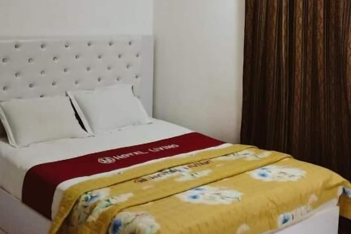 A bedroom with a bed, white headboard, and a window with curtains.