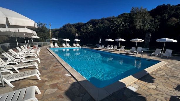 Una piscina con sillas de descanso y sombrillas, rodeada de baldosas de piedra y árboles.