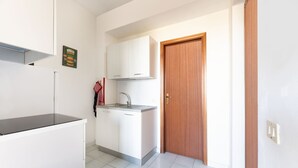 Una cocina compacta con armarios blancos, un lavamanos de acero inoxidable y una puerta de madera.