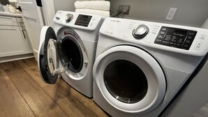 Een voorlader wasmachine en droger in een wasserette met houten vloer.