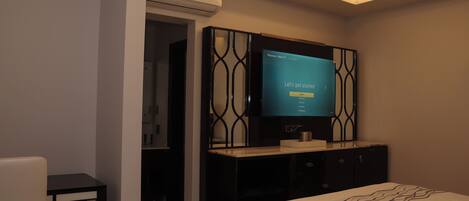 A modern hotel room with a bed, a TV mounted on a wall, a small table, and a wardrobe.