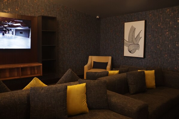Una sala de estar acogedora con una pared de diseño oscuro, un televisor de pantalla plana grande, un sofá cómodo con cojines amarillos y una obra de arte abstracta enmarcada.