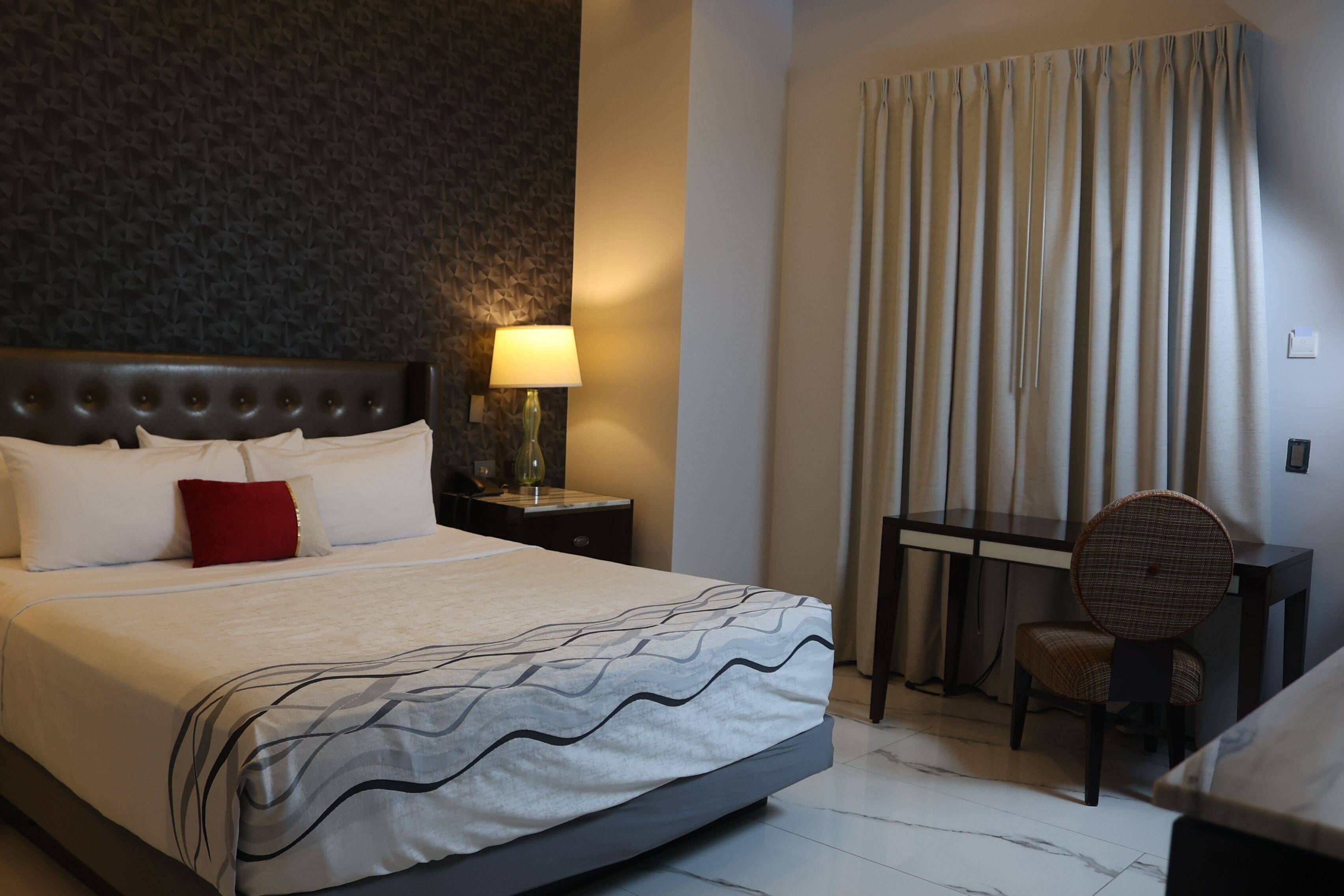 A hotel room with a large bed, a desk, a chair, and a lamp.