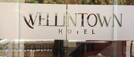 Letrero de hotel con el nombre "WELLINGTON HOTEL" y el reflejo de un vehículo y el interior.