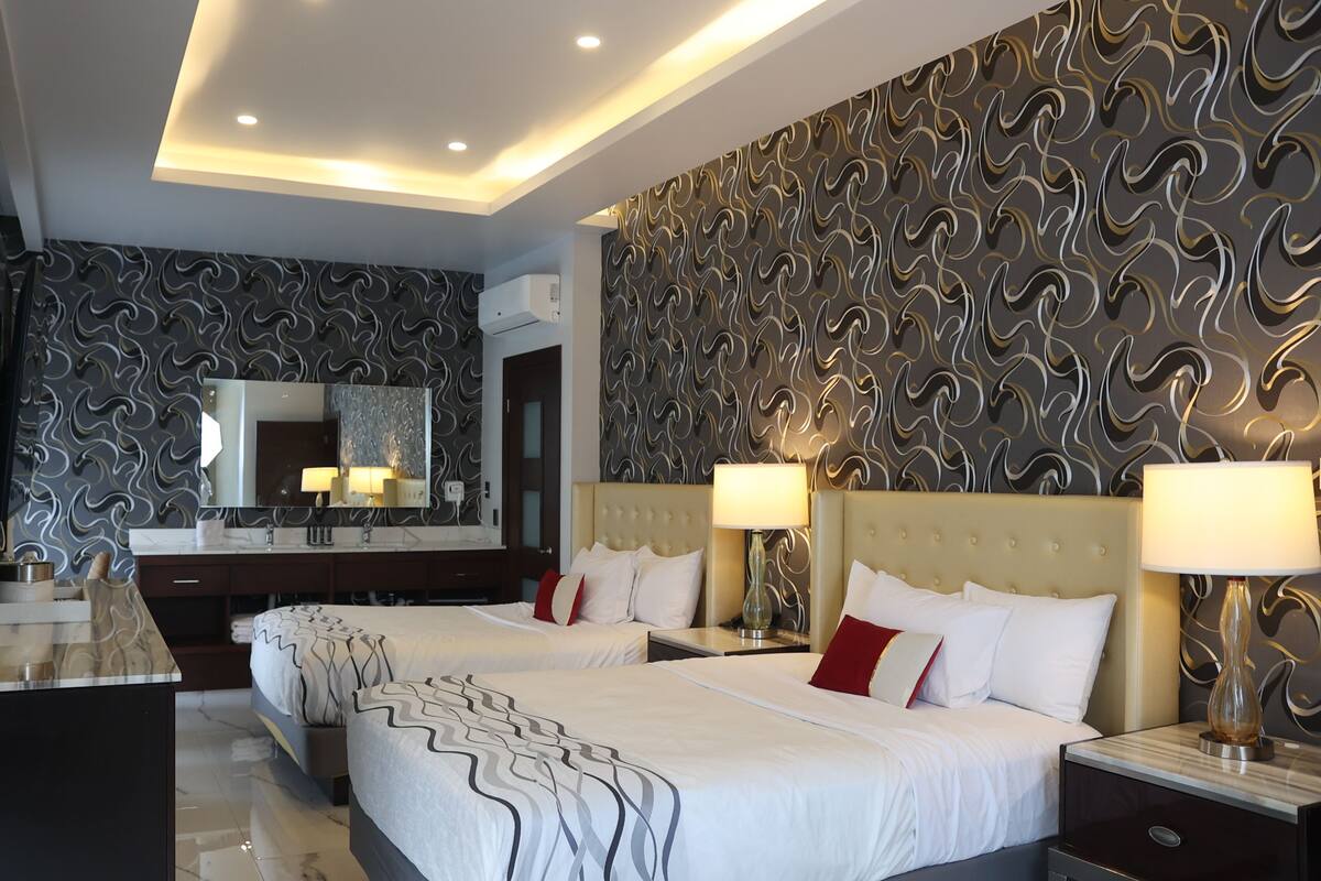 A hotel room with two beds, a large mirror, a vanity with a sink, and a patterned wall.