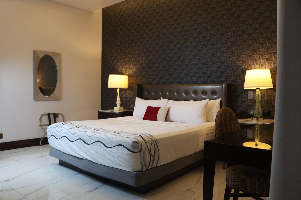 A hotel room with a large bed, two bedside tables with lamps, a chair, and a decorative wall piece.