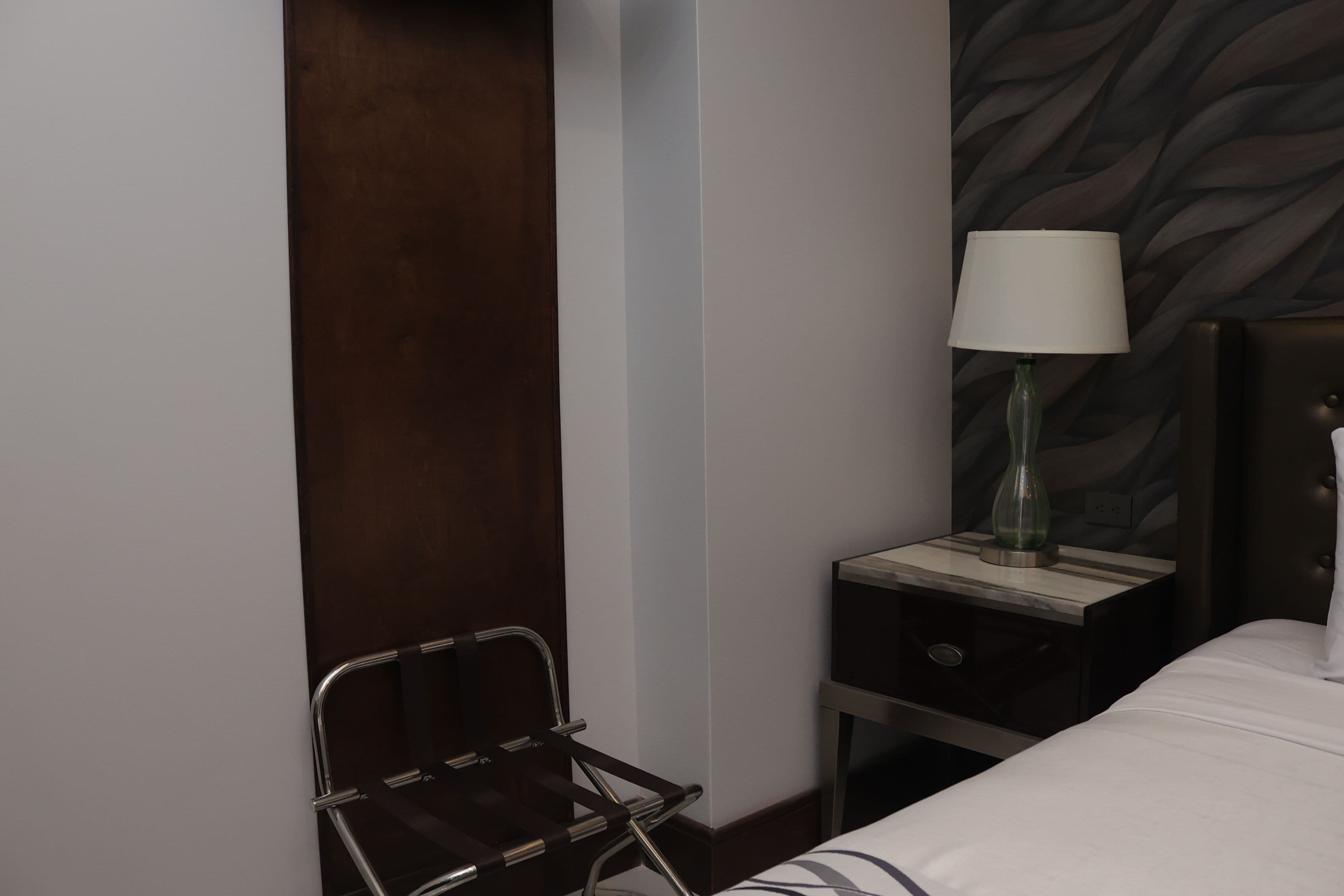 Habitación de hotel con cama, mesita de noche con lámpara, una silla y pared con diseño de hojas.