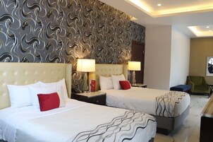 A hotel room with two beds, a patterned wall, and a green armchair.