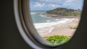 A view through a window of a beach with clear skies and calm waters. - Oceans 8 - Oceanstays -Absolute Oceanfront with Fireplace (Yamba)
