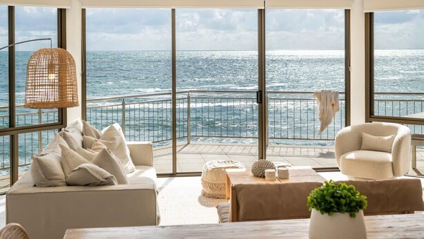 A spacious balcony with a view of the ocean, furnished with a sofa, armchairs, and a table with decorative items. - Oceans 8 - Oceanstays -Absolute Oceanfront with Fireplace (Yamba)