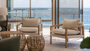 A balcony with two beige chairs and wicker ottomans, overlooking a coastal view. - Oceans 8 - Oceanstays -Absolute Oceanfront with Fireplace (Yamba)