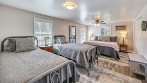 Ein Schlafzimmer mit drei Metallbetten, einem Deckenventilator und einem großen Fenster mit Jalousien.