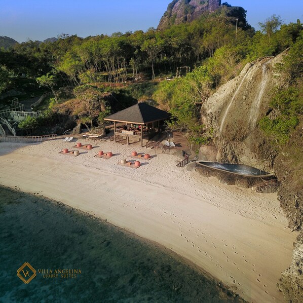 Una villa frente a la playa con una zona de estar cubierta, piscina y cascada.