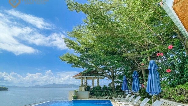 A swimming pool with a view of the sea, lounge chairs, and umbrellas. - Villa Angelina Luxury Suites (Dapitan)