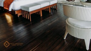 A hotel room with a large bed, a sofa, a wicker chair, and a dining table. - Villa Angelina Luxury Suites (Dapitan)