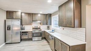 Uma cozinha moderna com eletrodomésticos de aço inoxidável, armários de madeira e painel de azulejos brancos.