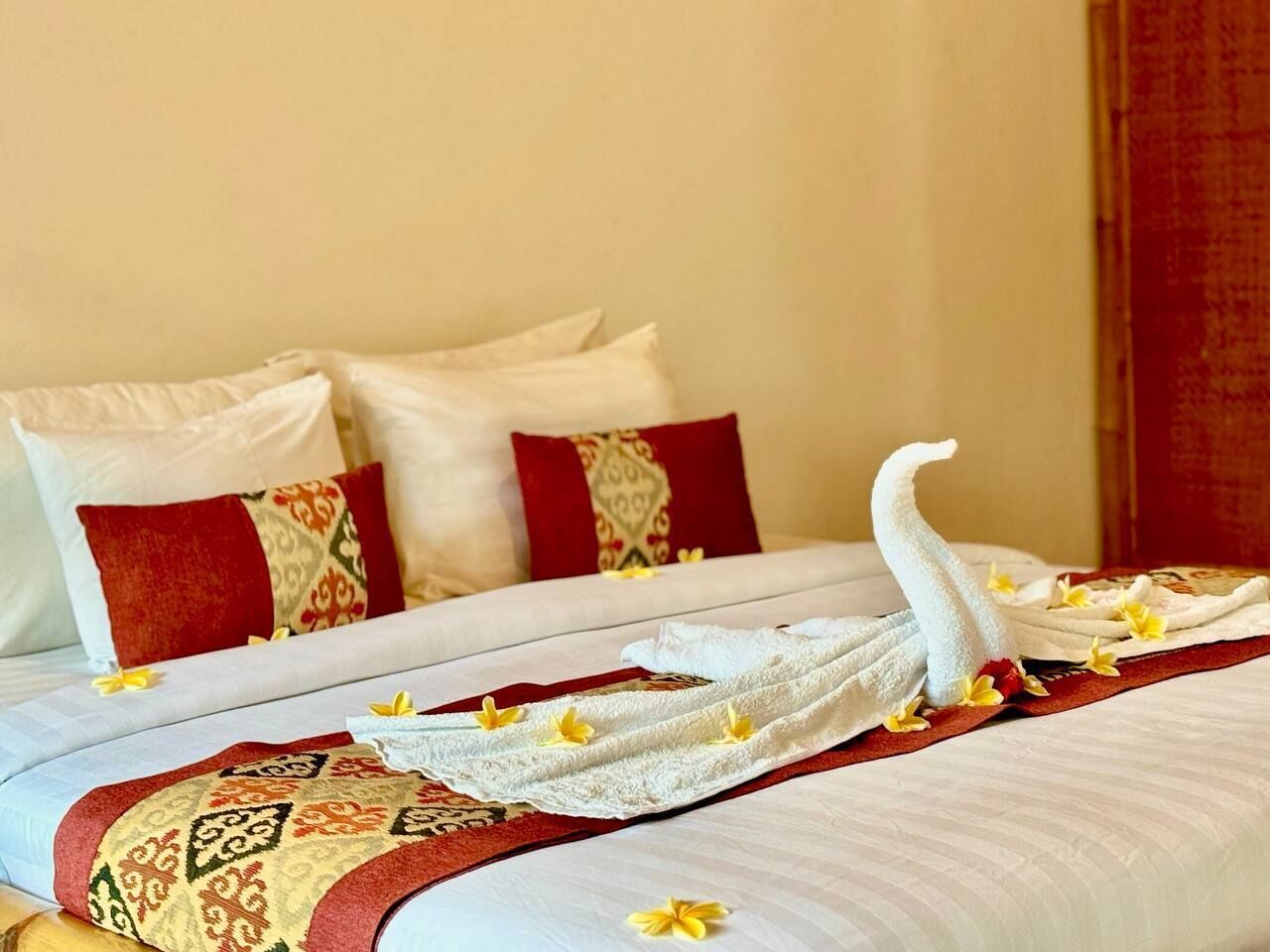 A neatly made bed with a patterned bedspread, pillows with decorative pillows, and a towel arranged in a swan shape with flowers.