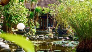 A traditional building with a tiled roof, surrounded by lush greenery and a pond with lily pads and flowers. - Narafa's Guest House (Karangasem)