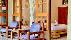 A room with a bed, two wooden chairs with blue cushions, and a window with a curtain. - Narafa's Guest House (Karangasem)