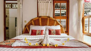 Una cama bien hecha con ropa de cama blanca y a rayas, almohadas rojas y estampadas, y una toalla con flores amarillas.