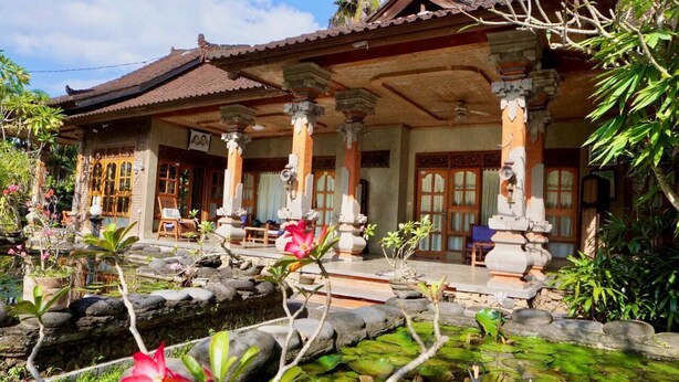 A traditional wooden house with a tiled roof, stone pillars, and a garden with a pond and plants. - Narafa's Guest House (Karangasem)