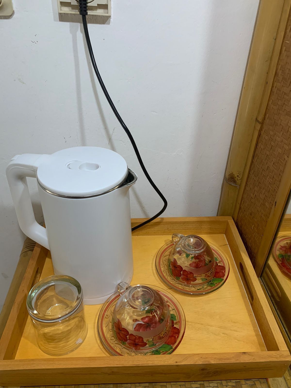 Una tetera eléctrica blanca sobre una bandeja de madera con dos vasos de vidrio y un tarro de vidrio.
