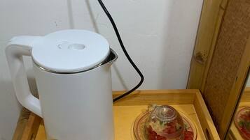 Una tetera eléctrica blanca sobre una bandeja de madera con dos vasos de vidrio y un tarro de vidrio.