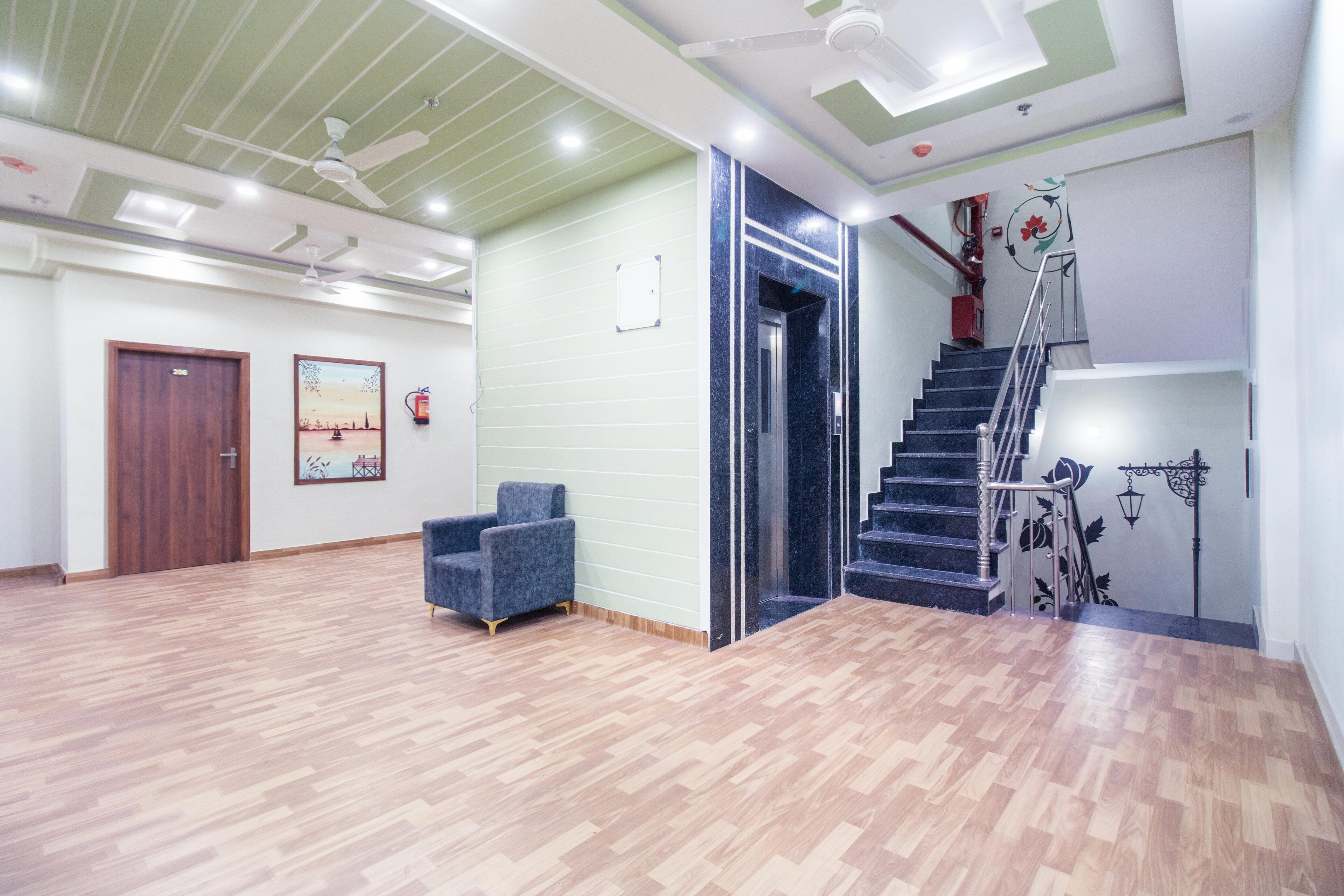 A spacious lobby with a wooden floor, a blue armchair, a staircase with a metal railing, and a ceiling fan.