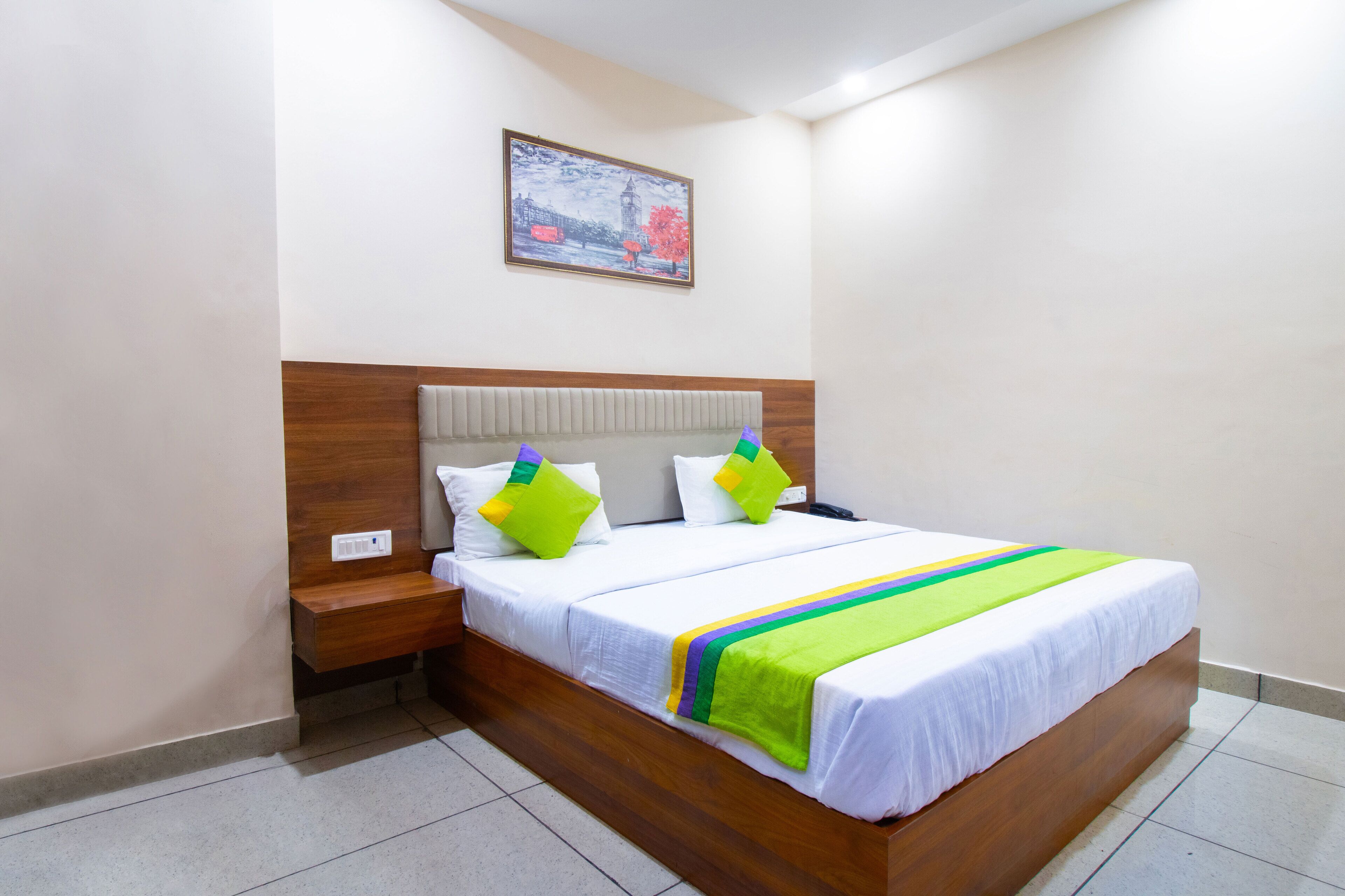A neatly made bed with white bedding and a colorful striped blanket, a wooden headboard, and a nightstand with a phone.