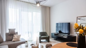A modern living room with a sofa, a coffee table, a TV, and a decorative vase with flowers. - Luxurious 1BR Oasis Panoramic Views (Dubai)