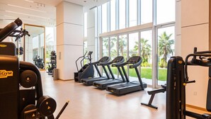 A gym with treadmills, weight machines, and a large window offering a view of palm trees. - Luxurious 1BR Oasis Panoramic Views (Dubai)