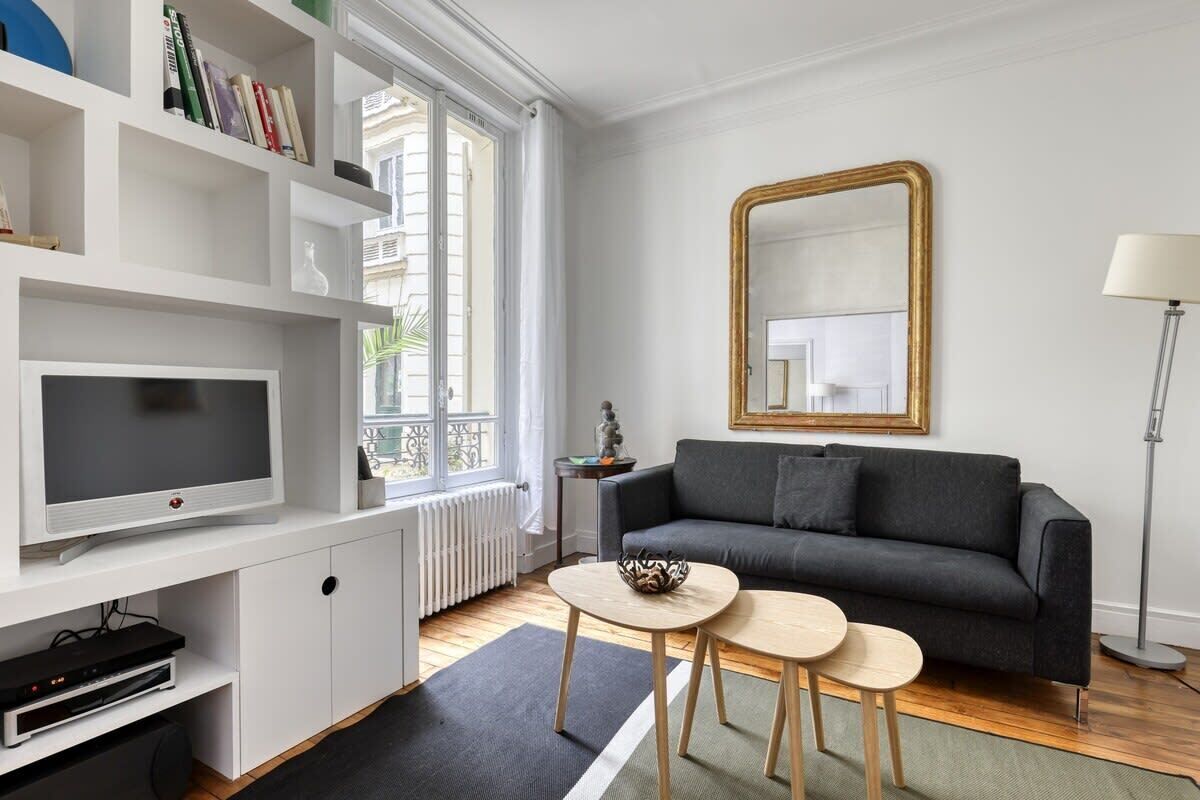 A modern living room with a grey sofa, a TV, a bookshelf, and a large mirror.