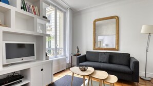 Una sala de estar moderna con un sofá gris, un televisor, una estantería y un espejo grande.