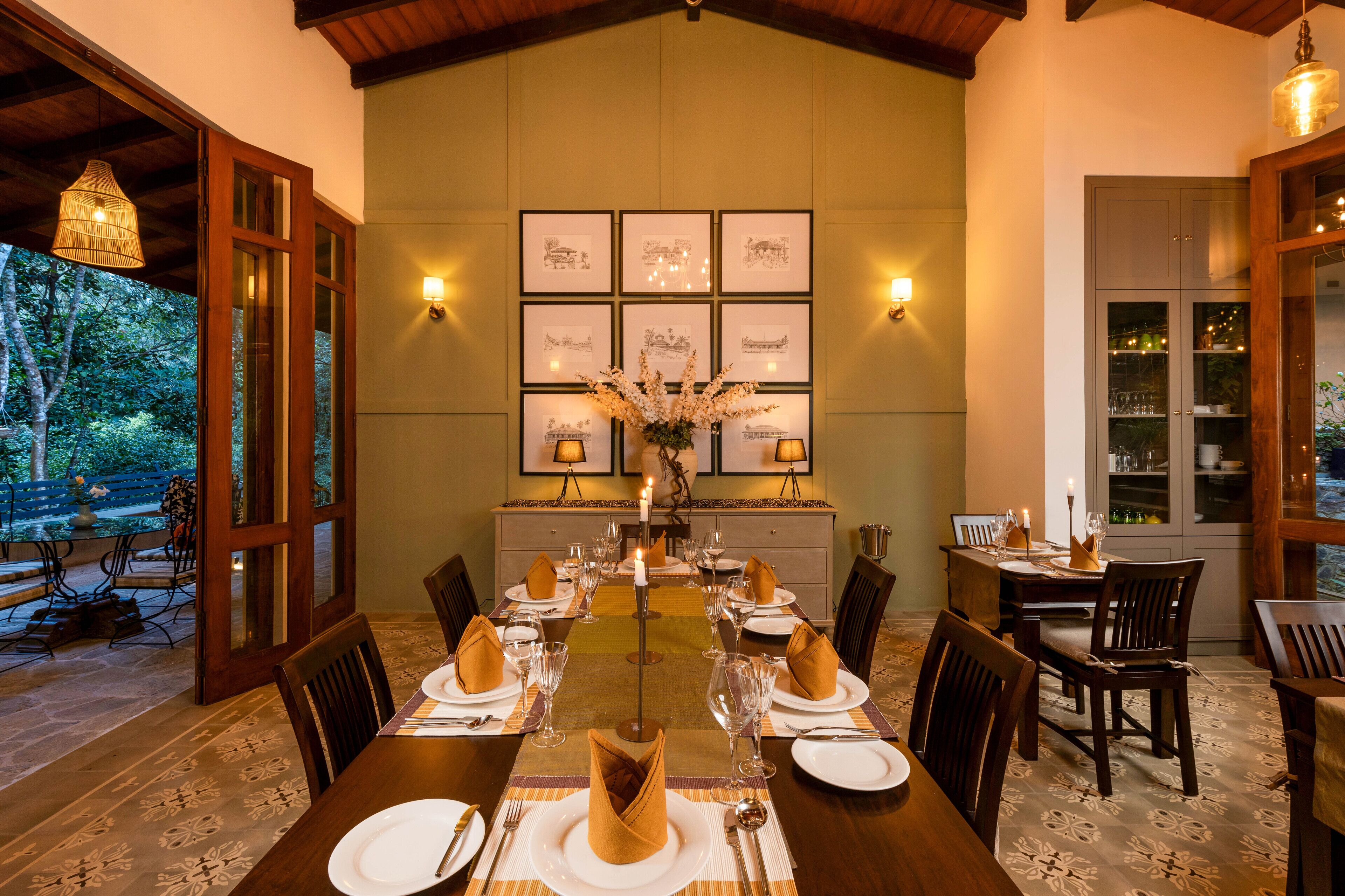 A dining area with a long table set for a meal, surrounded by chairs, with framed artwork on the wall and a vase with flowers in the center.