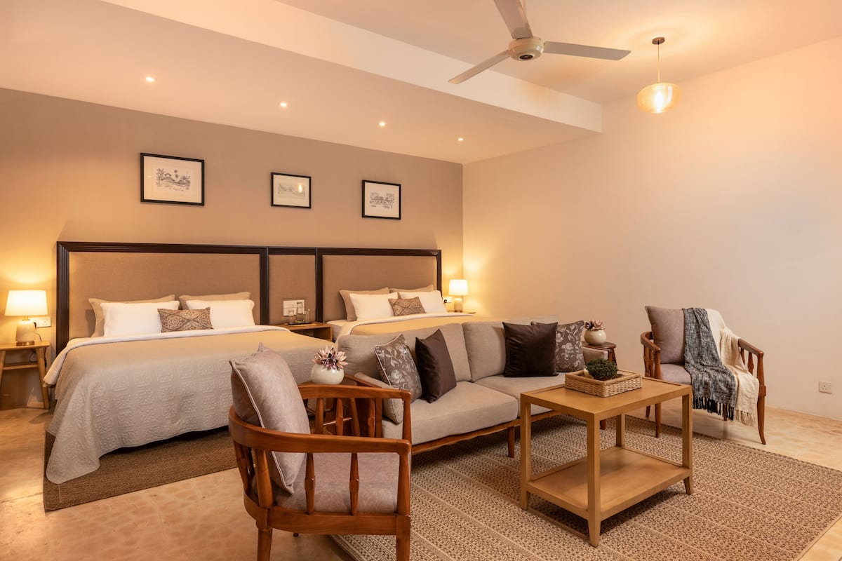 A hotel room with a large bed, a sofa, a chair, a table, and a ceiling fan.