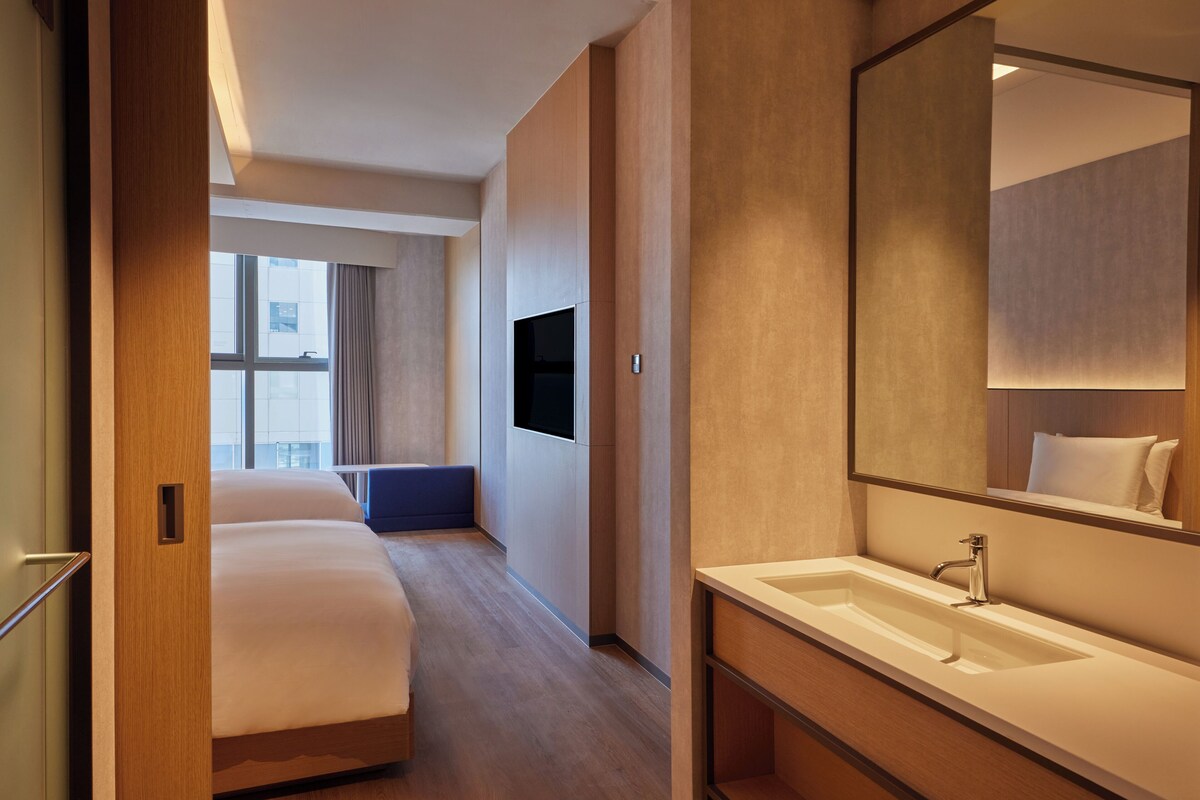 Een hotelkamer met een groot bed, een badkamer met spiegel en wastafel, en een aan de muur bevestigde televisie.