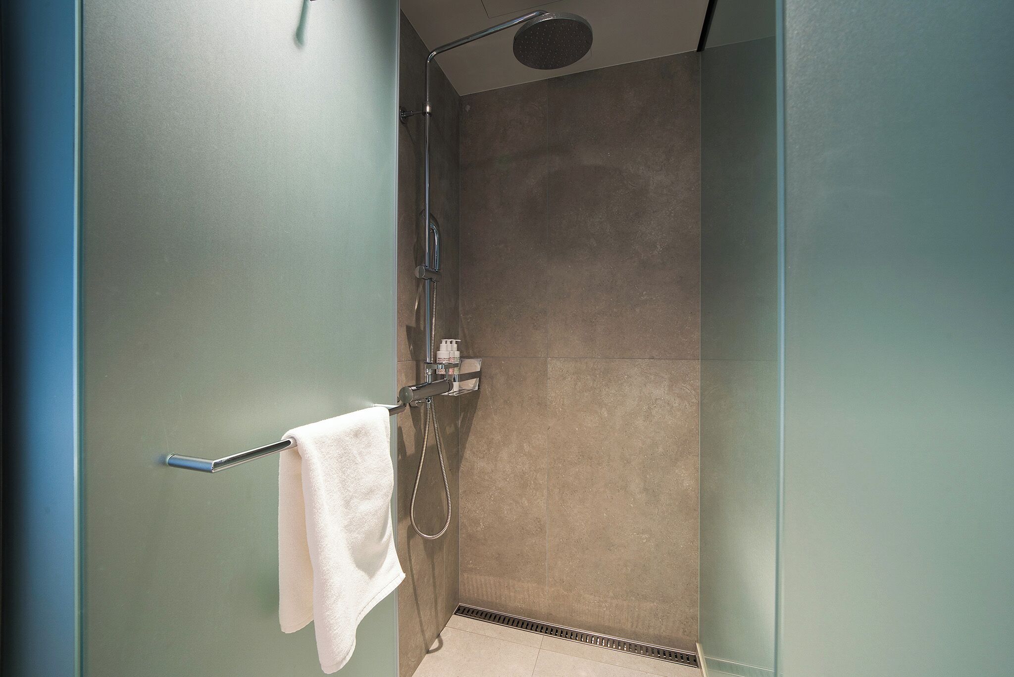 Une douche moderne équipée d’un pommeau de douche à main, d’un porte-serviettes avec une serviette blanche et d’un panneau de commande fixé au mur.