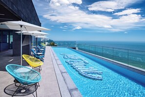 A rooftop infinity pool with a clear view of the ocean, surrounded by colorful chairs and umbrellas.