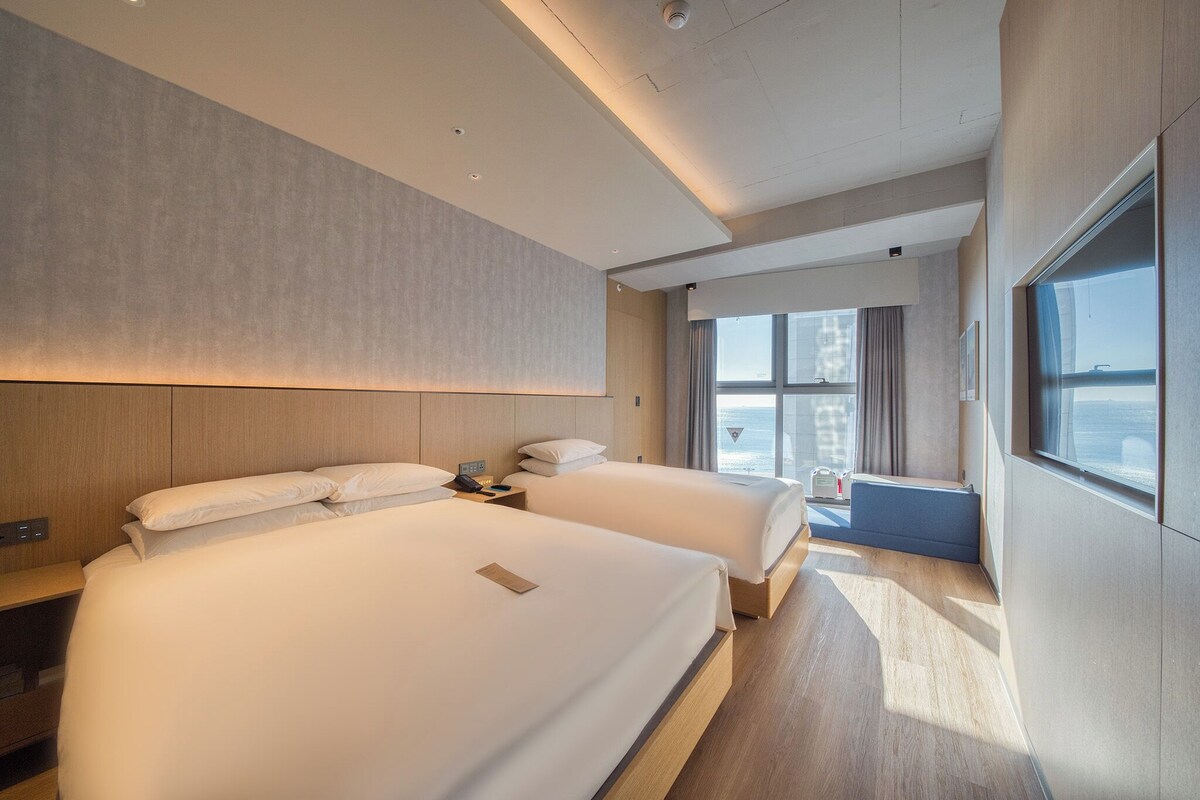 Een moderne hotelkamer met twee bedden, een groot raam met uitzicht en een houten vloer.