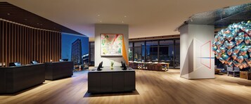 A modern hotel lobby with a reception desk, a central island, and a large window offering a city view.